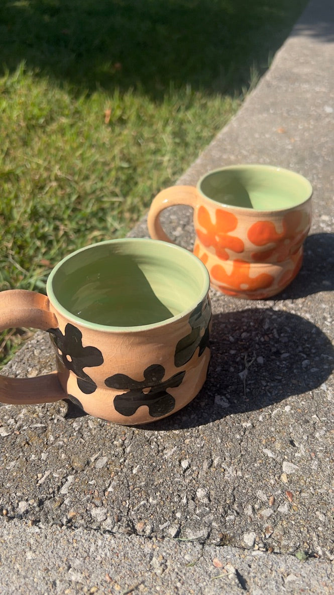 Two ceramic mugs with floral designs on a concrete surface.