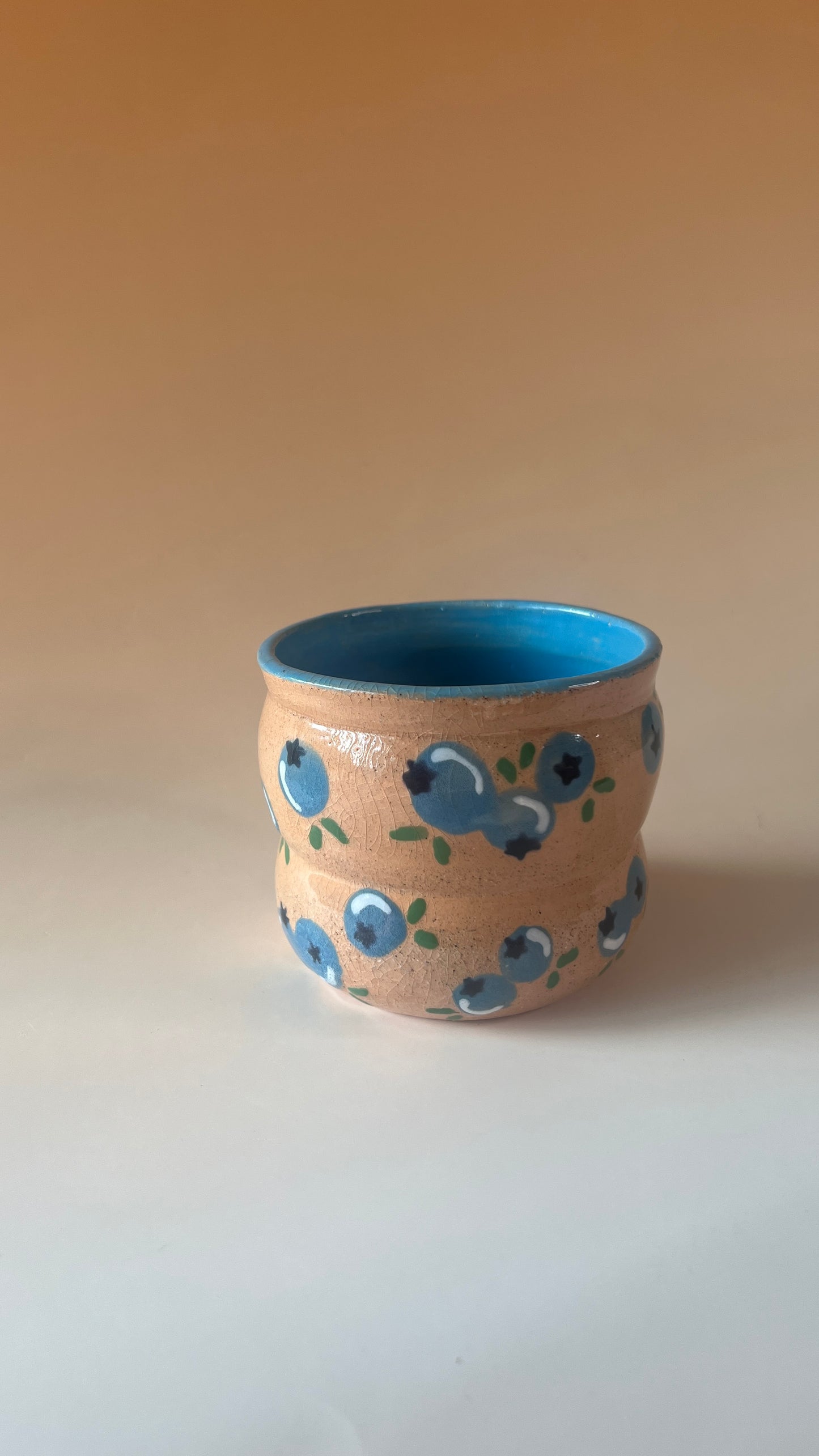 Ceramic cup with blue berry patterns on a beige background