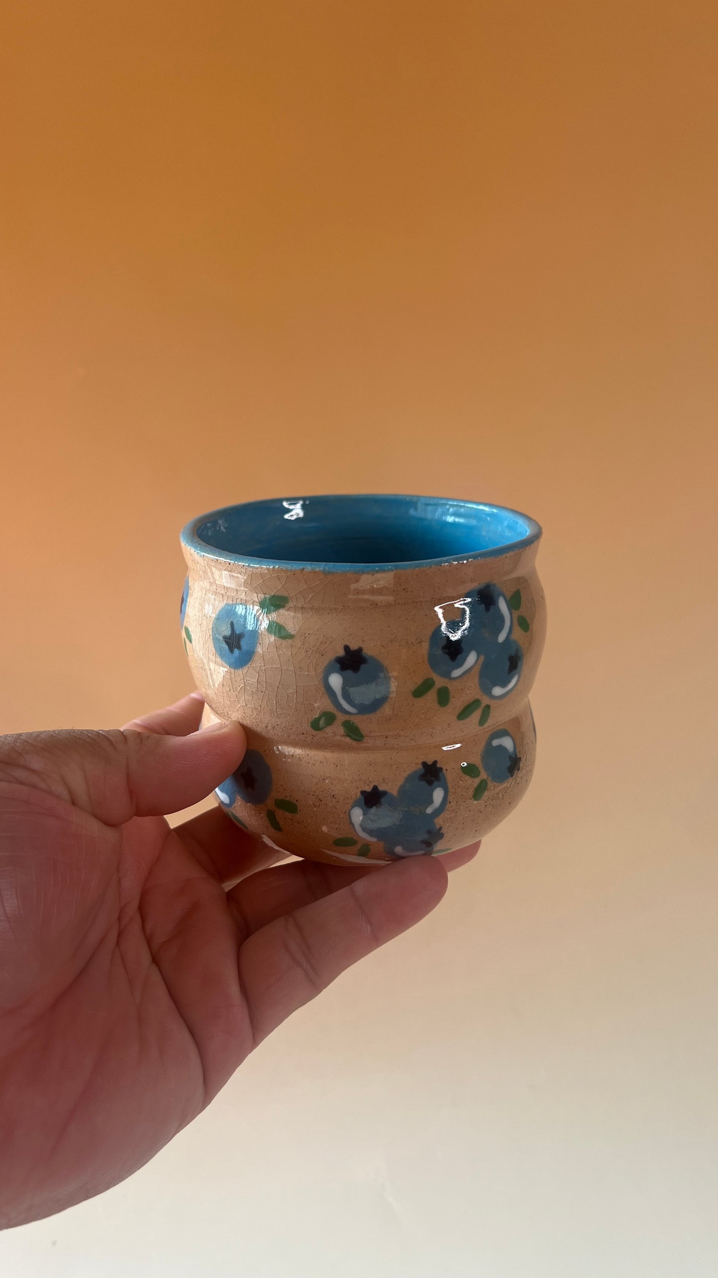 Hand holding a ceramic cup with blue interior and decorative patterns on an orange background
