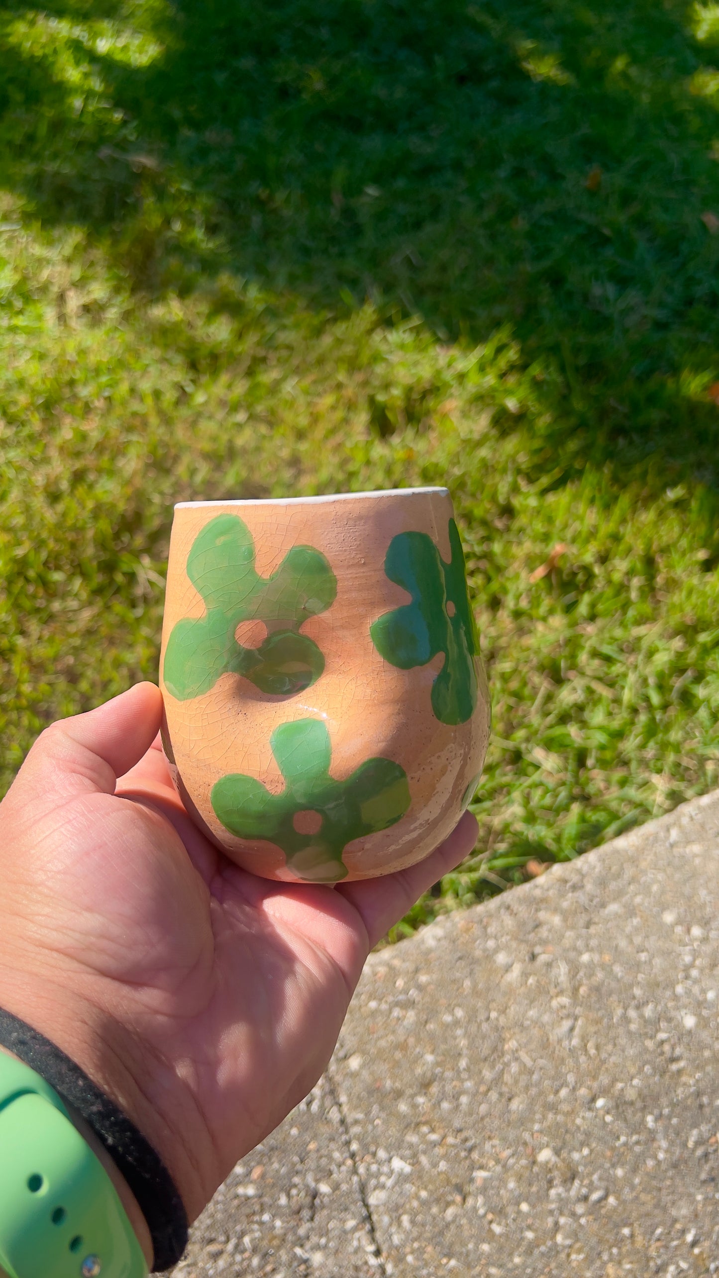Hand holding a pink ceramic cup with green floral patterns against a grassy background