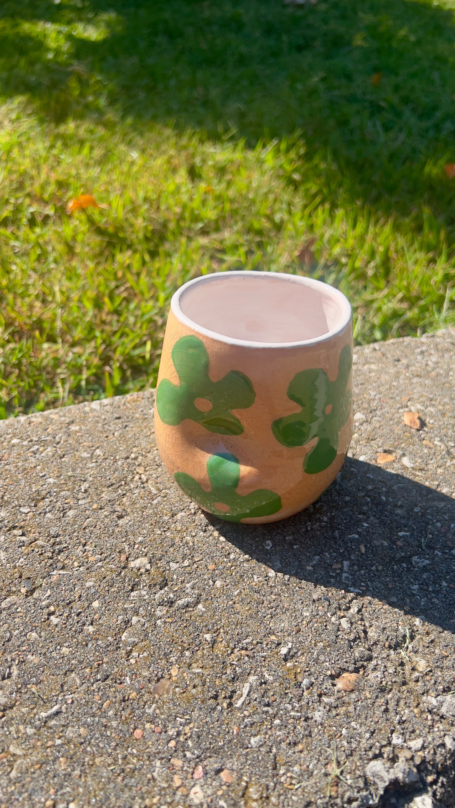 Ceramic mug with green abstract pattern on a concrete surface with grass in the background