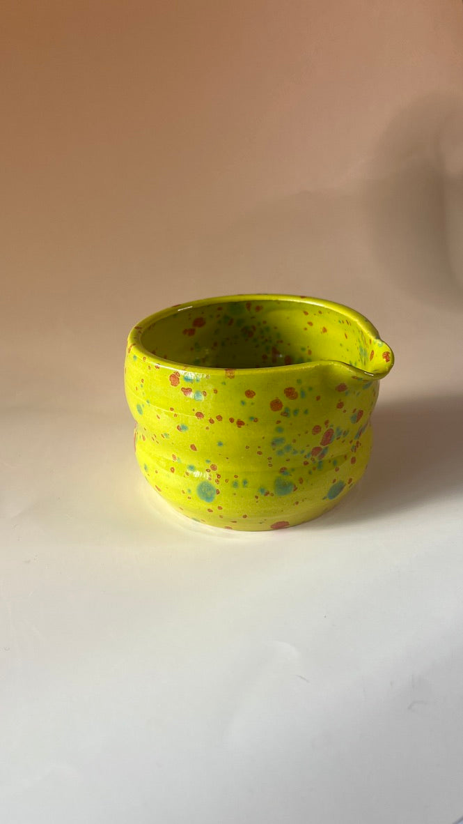 Neon green ceramic cup with colorful speckles on a beige background