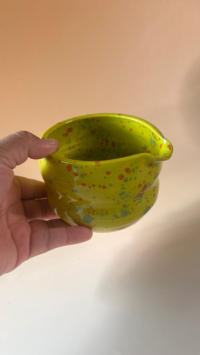 Hand holding a small green neon ceramic pot with colorful speckles against a plain background