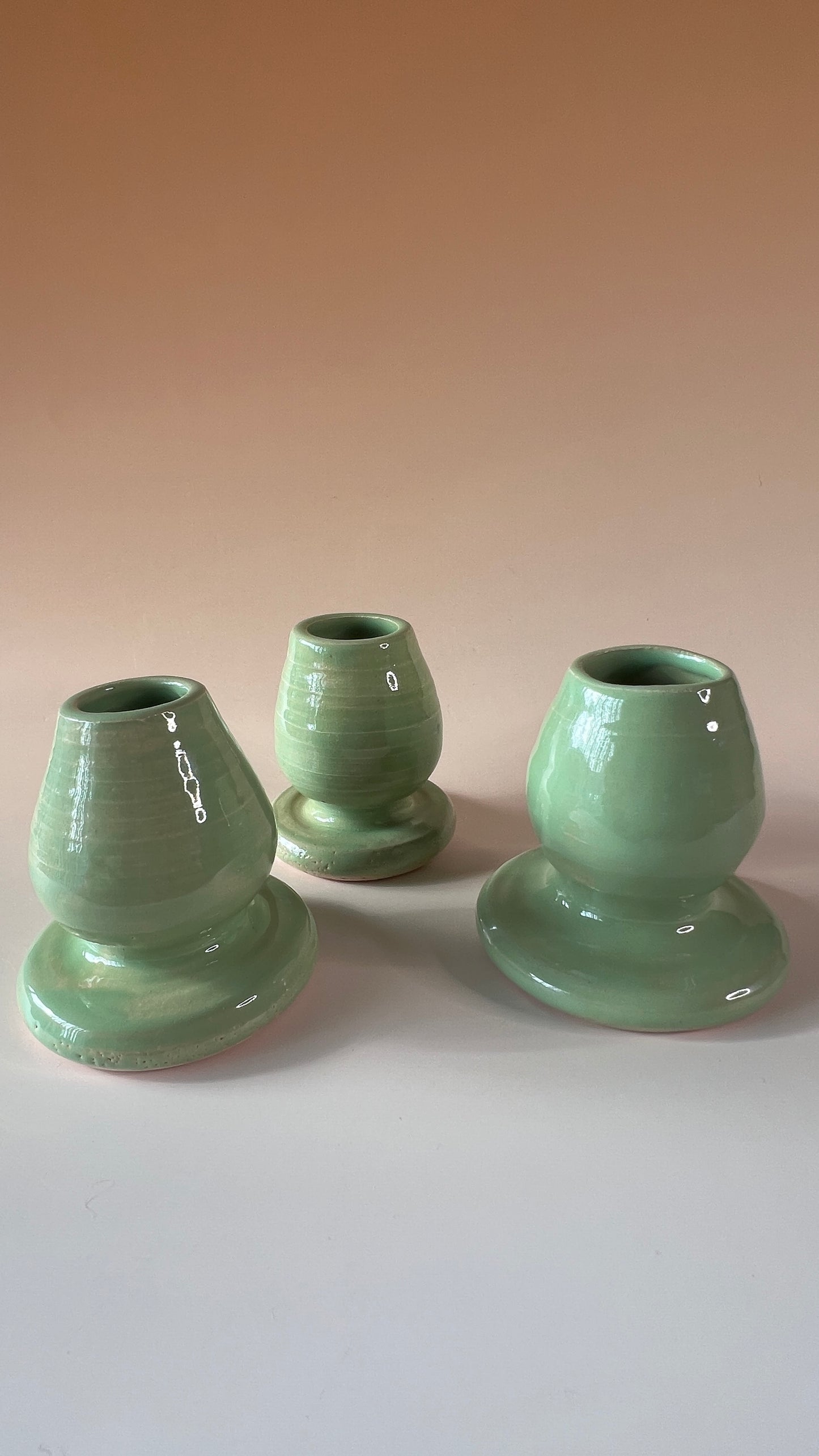 Three green ceramic candle holders on a white surface with a beige background
