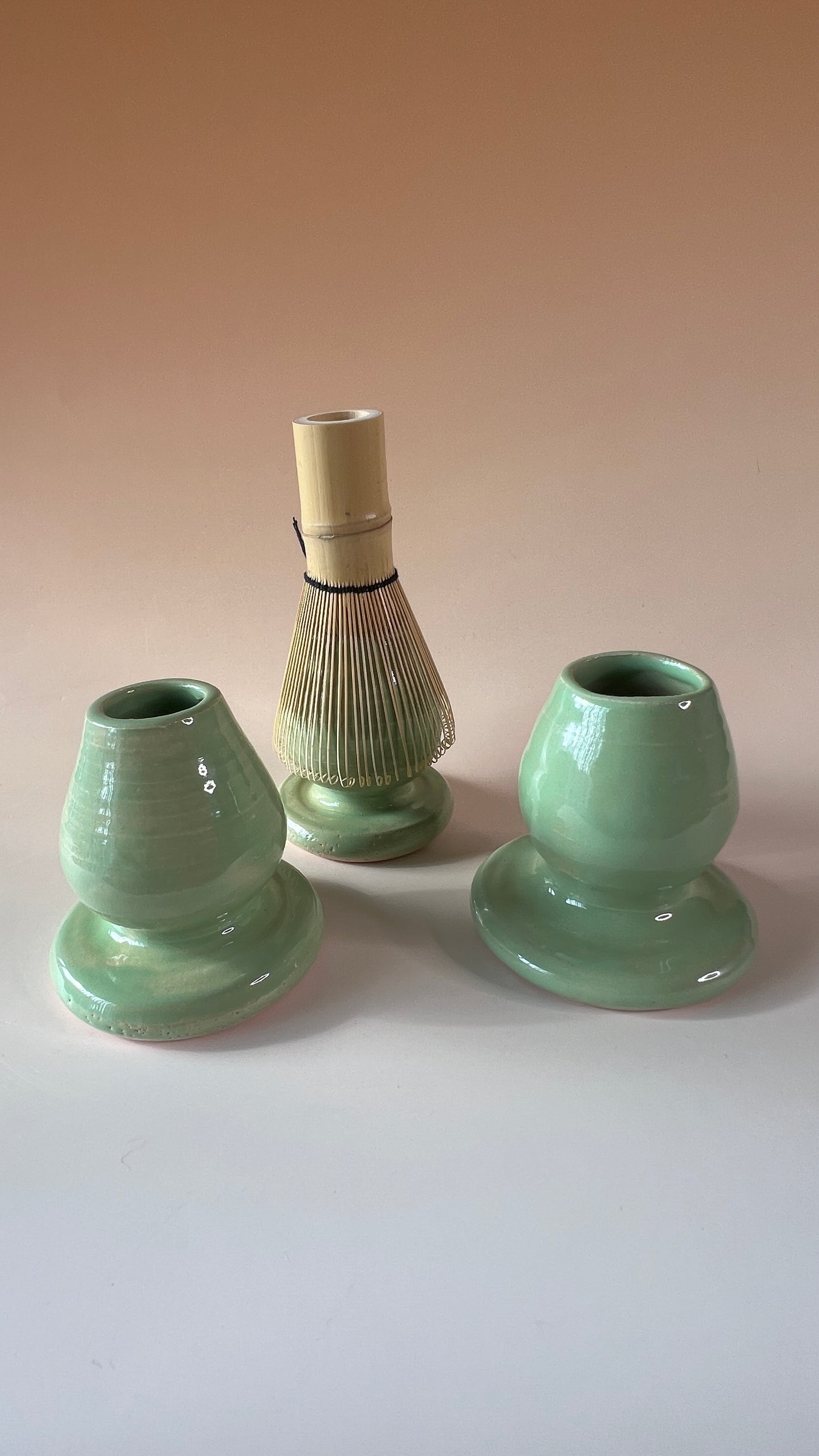 Three pieces of green ceramic matcha whisk holders on a beige background