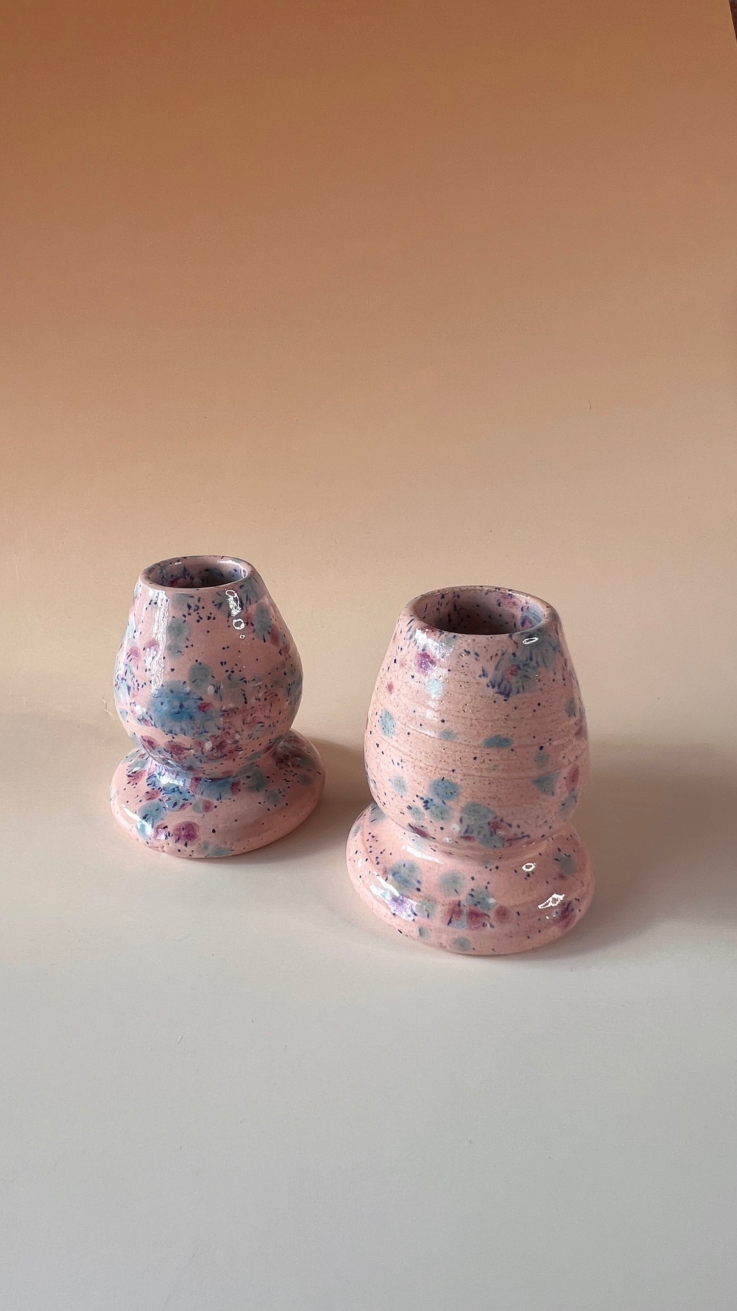 Two pink ceramic matcha whisk holders with colorful blue, pink, and white speckles on a beige background