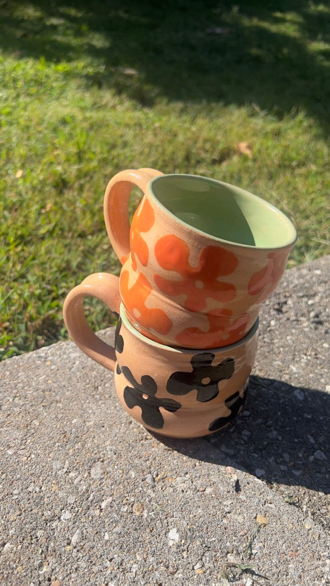 Two ceramic mugs stacked on a concrete surface with grass in the background