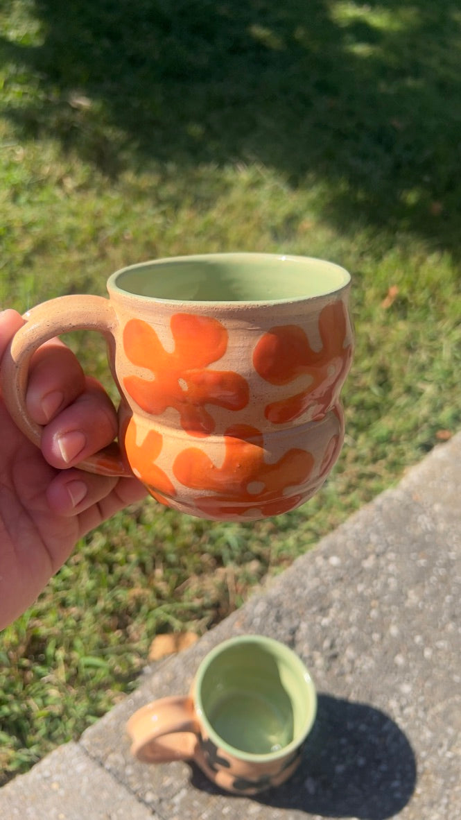 Hand holding a ceramic mug with orange floral patterns on a grassy background