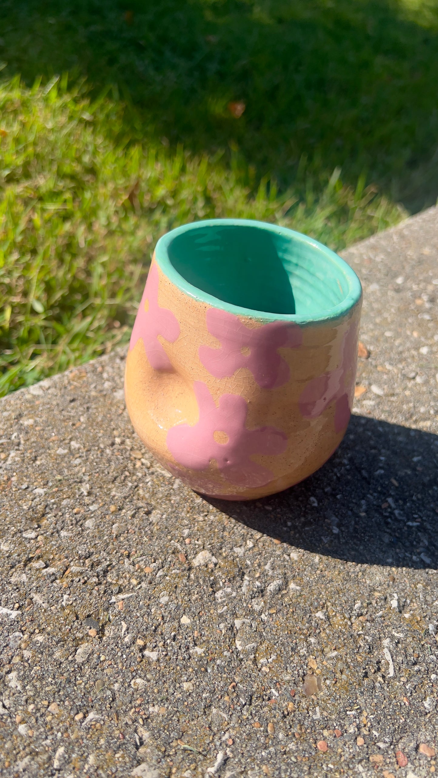 Ceramic cup with pink and green design on a concrete surface