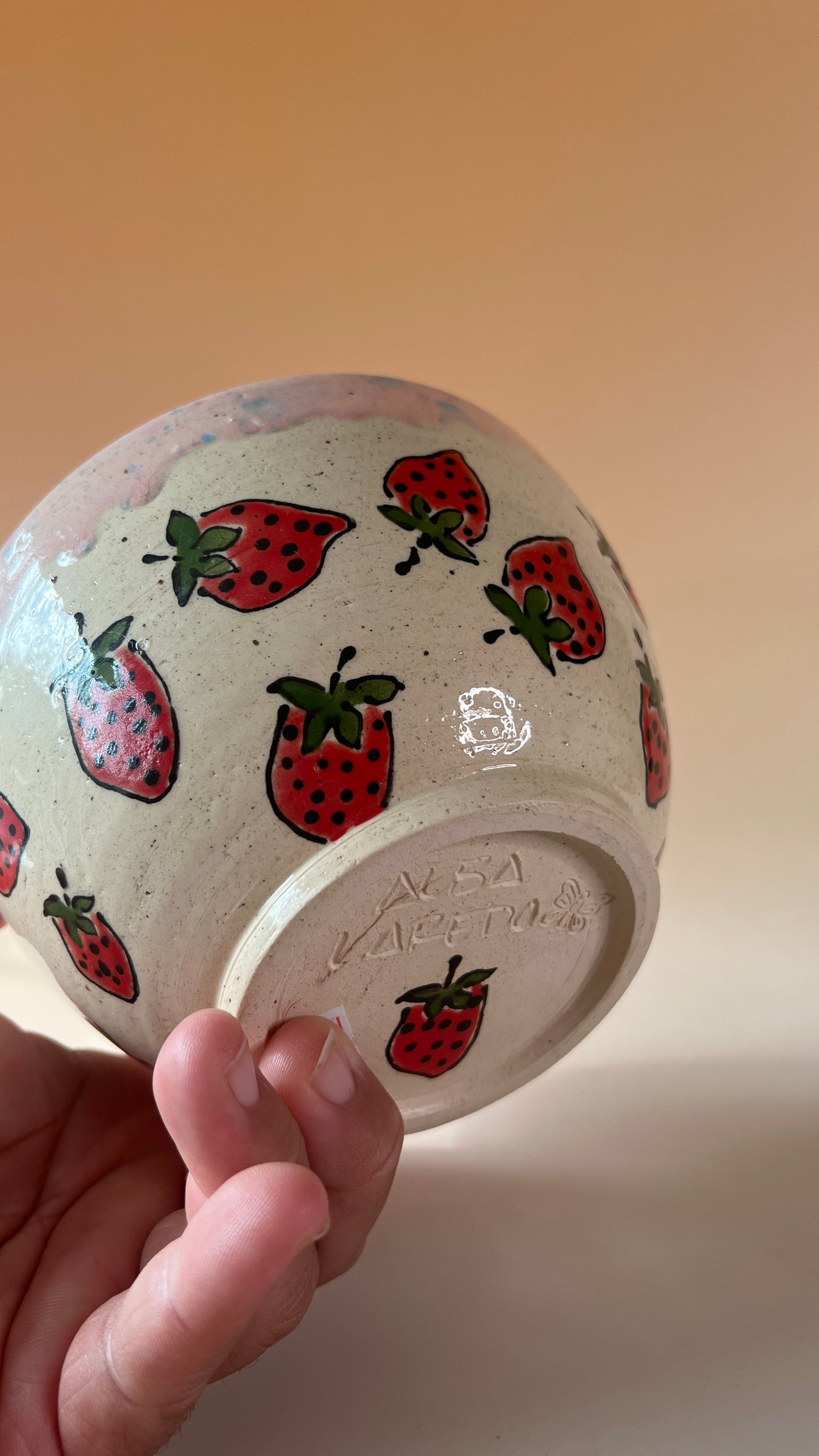 Ceramic bowl with strawberry pattern held by a hand against a beige background