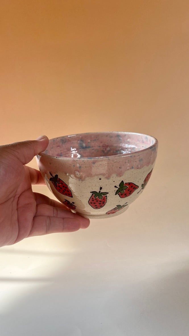 Hand holding a small ceramic bowl with strawberry pattern against a plain background