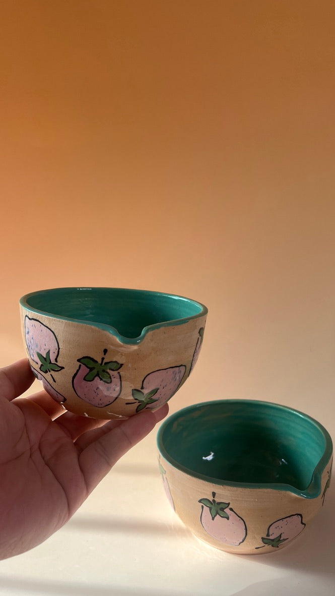 Handmade ceramic bowl with pink strawberries design and inside a held by a hand against a warm-toned background