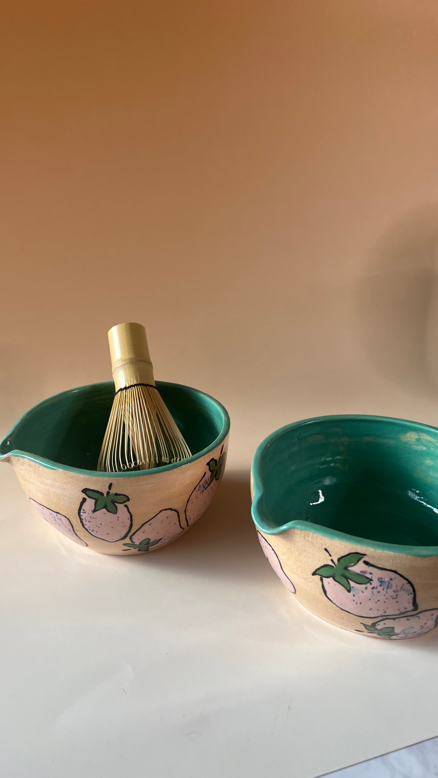 Two pink strawberry ceramic bowls design with a whisk on a plain background