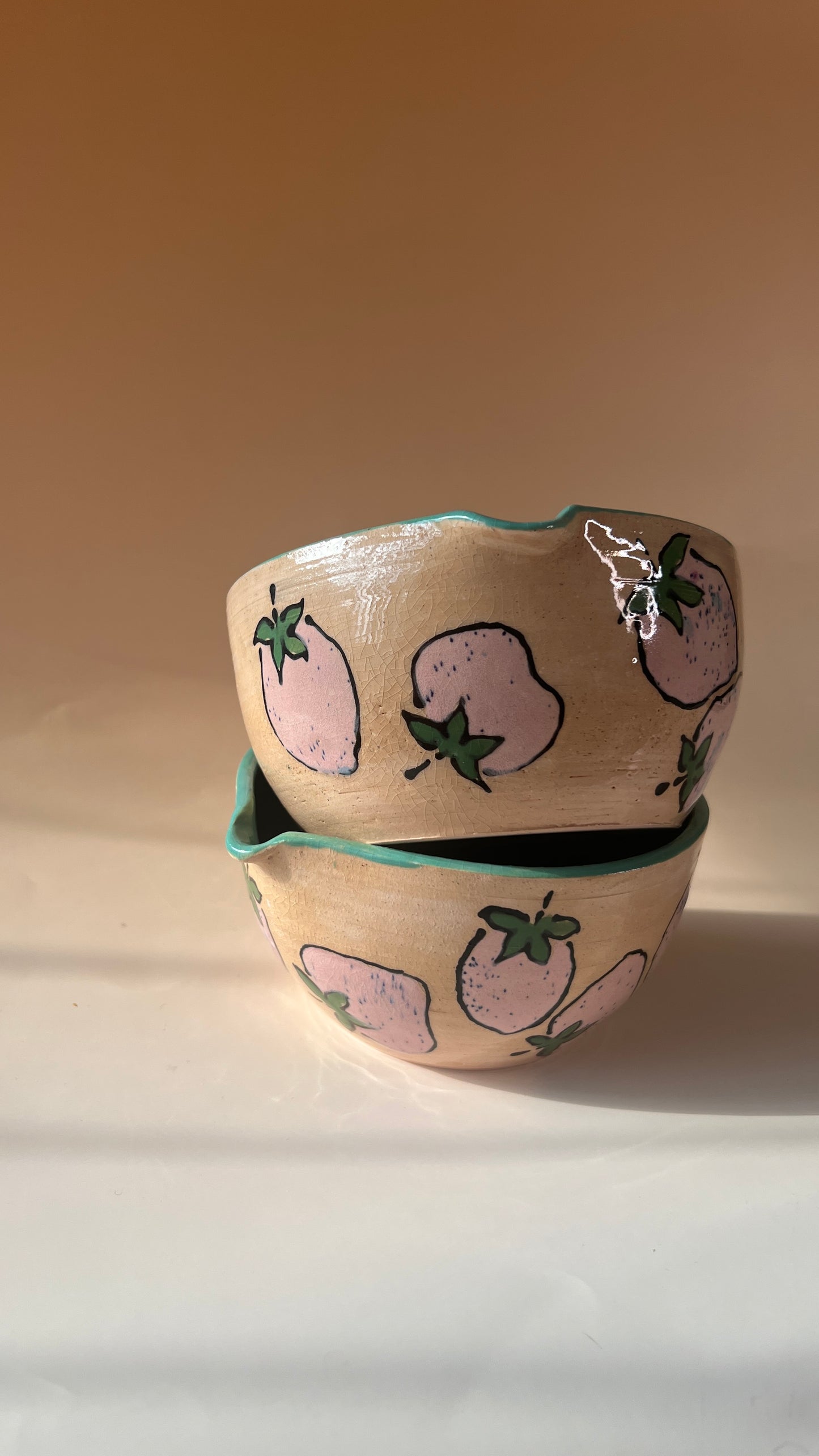 Two ceramic bowls with pink strawberry designs on a beige background