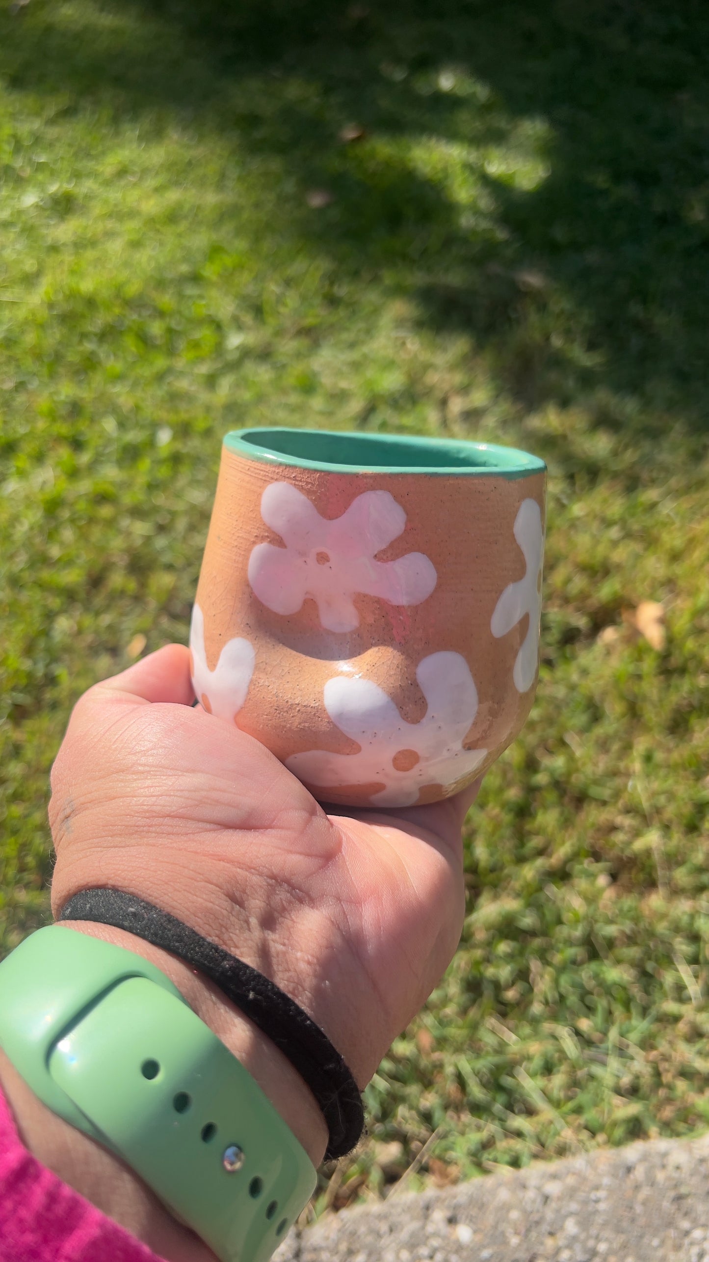 Hand holding a pink floral-patterned cup with a green rim against a grassy background