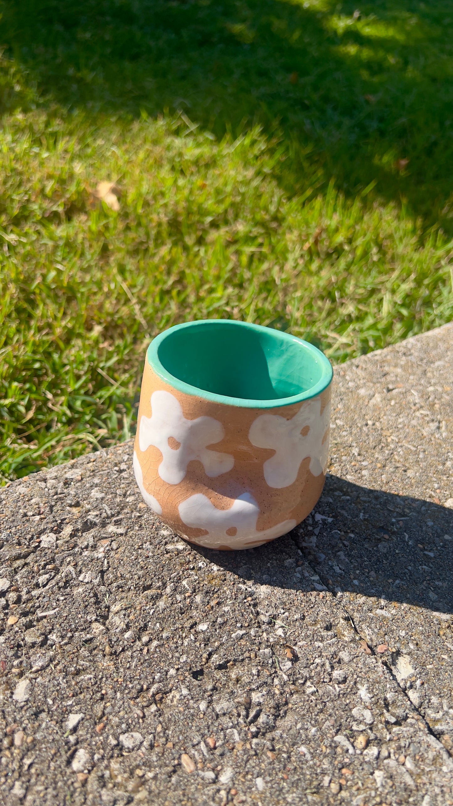 Ceramic mug with floral patterns on a concrete surface with grass in the background