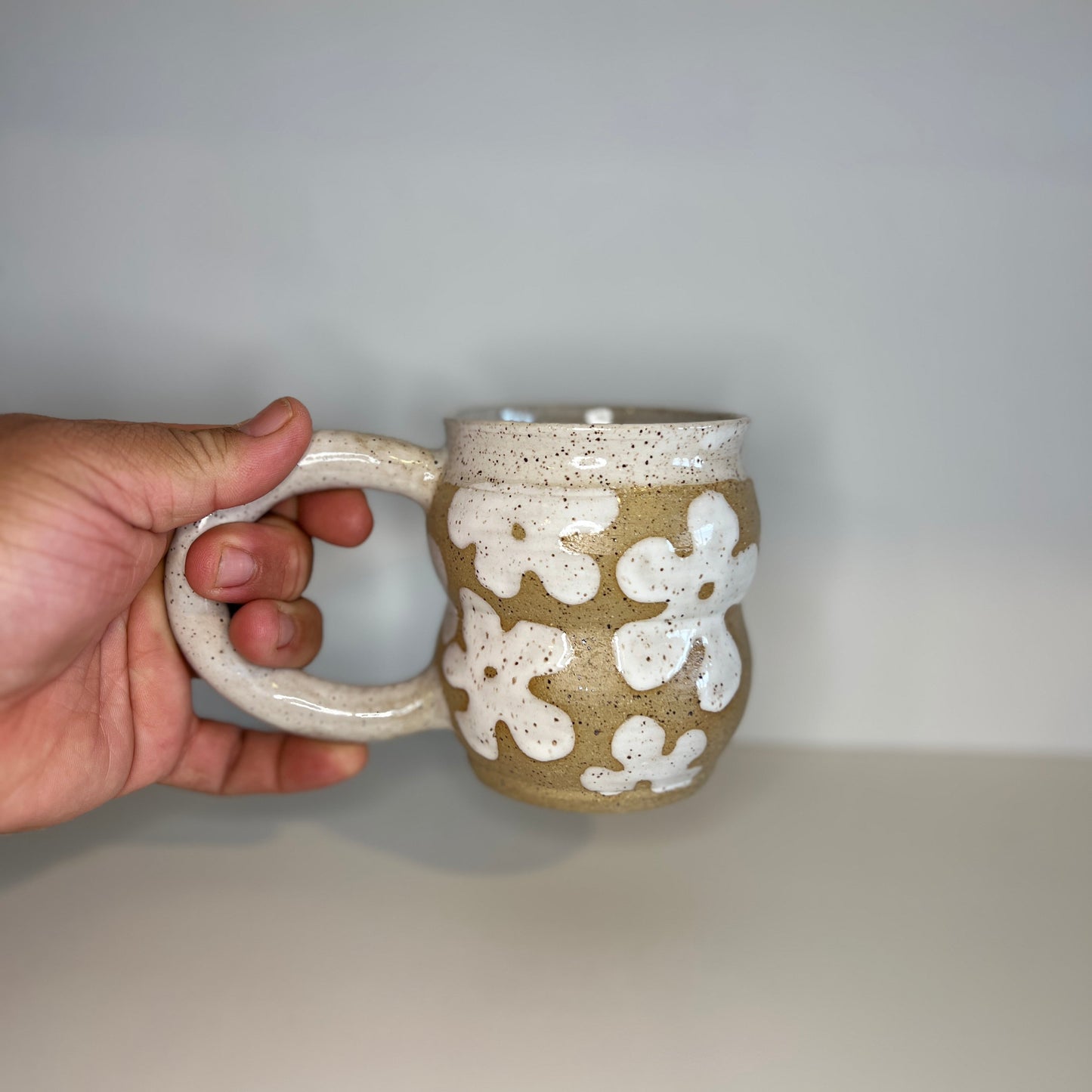 Hand holding a ceramic mug with white floral patterns against a plain background