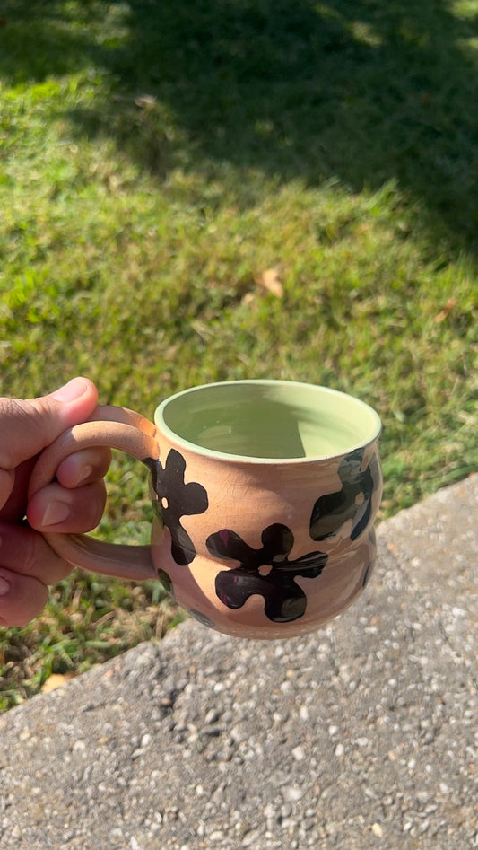 Person holding a ceramic mug with floral design outdoors