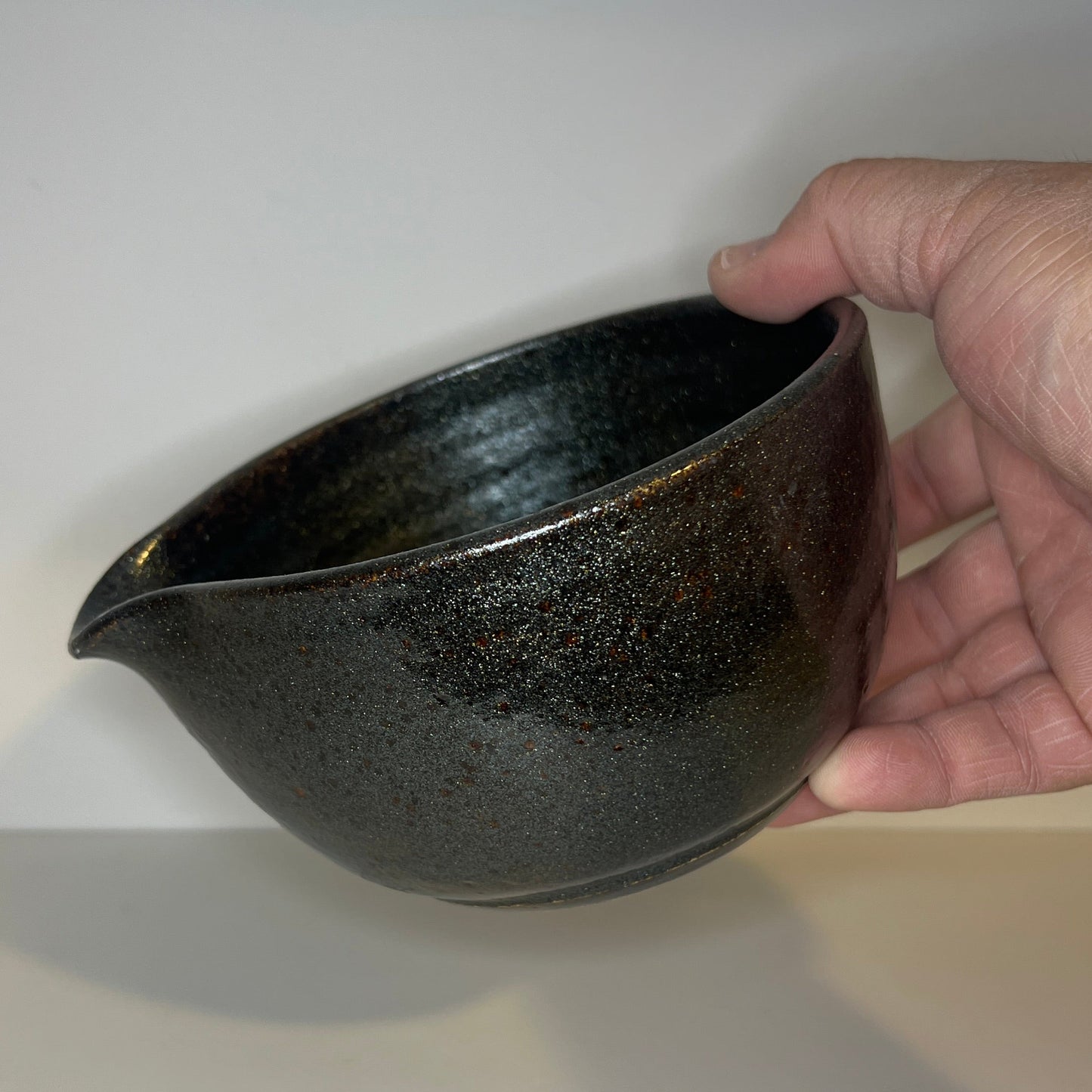 Hand holding a black ceramic bowl against a white background