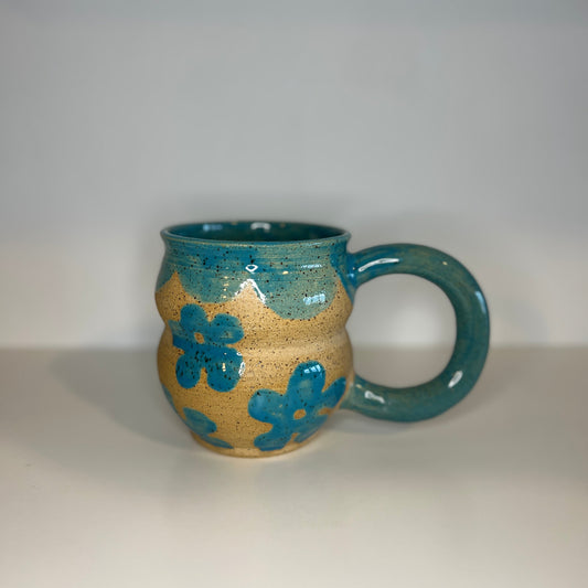 Ceramic mug with blue interior and floral patterns on beige exterior against a white background