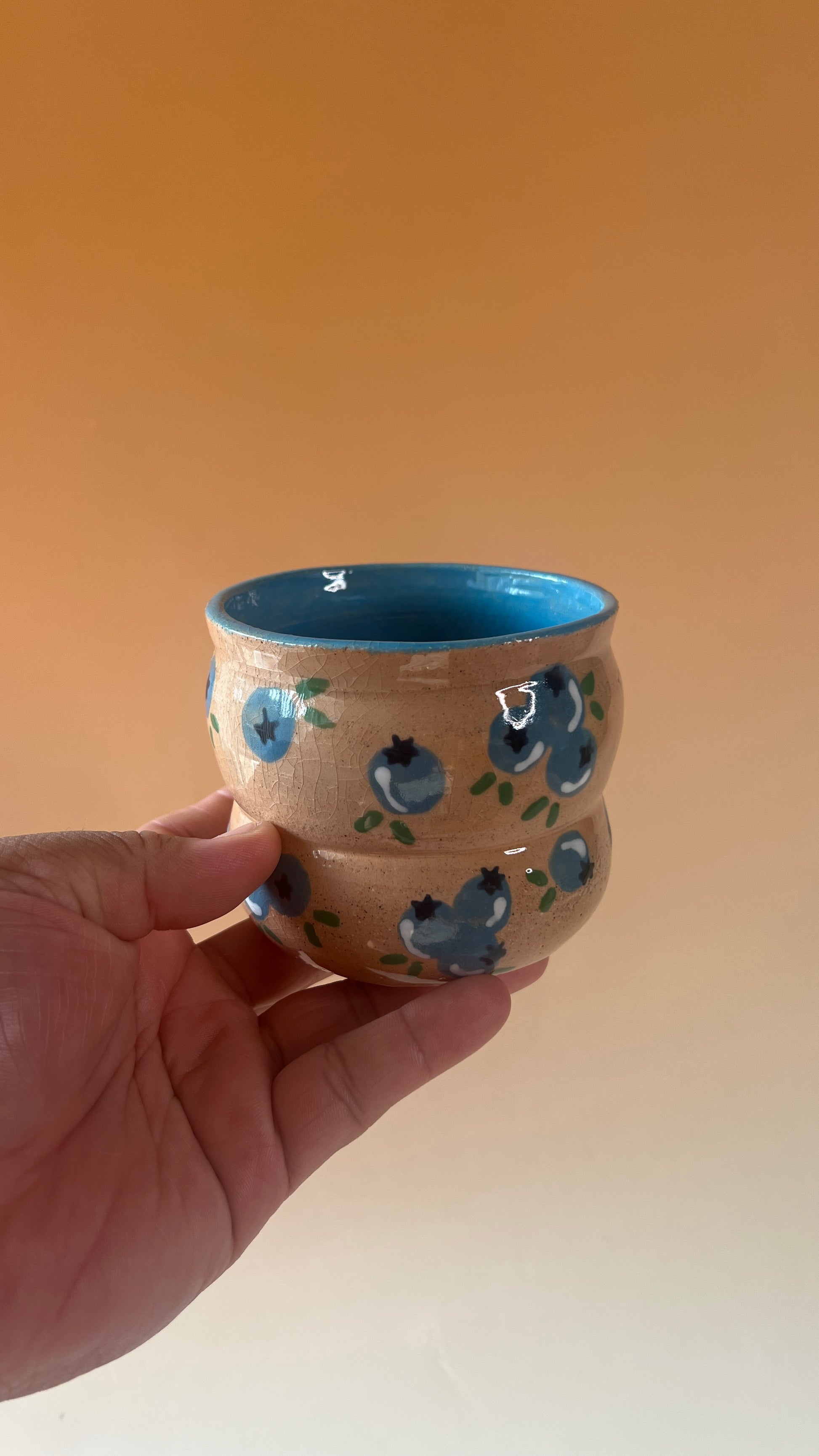 Hand holding a ceramic cup with blue interior and decorative patterns on an orange background