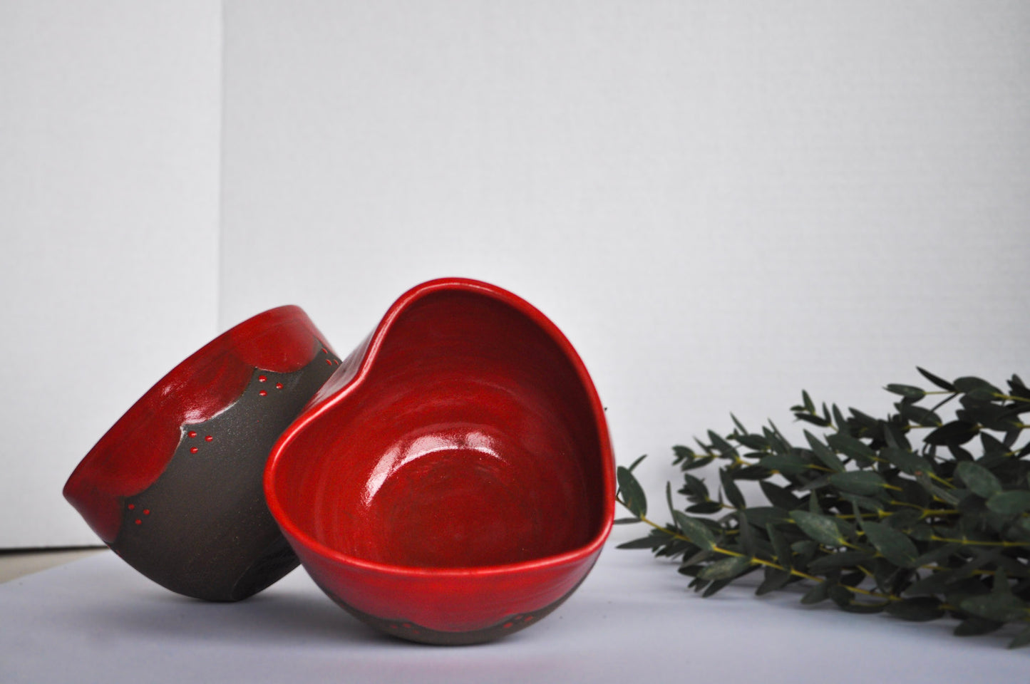 Red ceramic bowls on a light surface with green leaves in the background