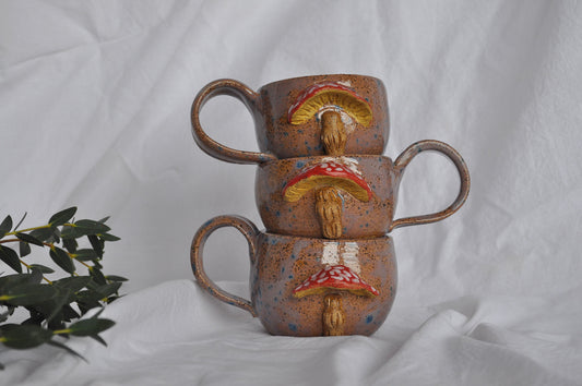 Stack of three ceramic mugs with mushroom designs on a white background