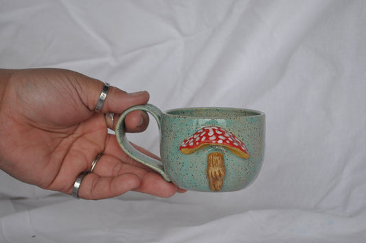 Hand holding a ceramic mug with a mushroom design against a white background