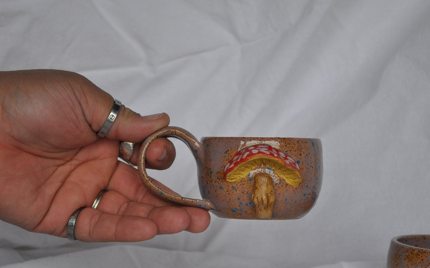 Hand holding a ceramic mug with a decorative design against a plain background