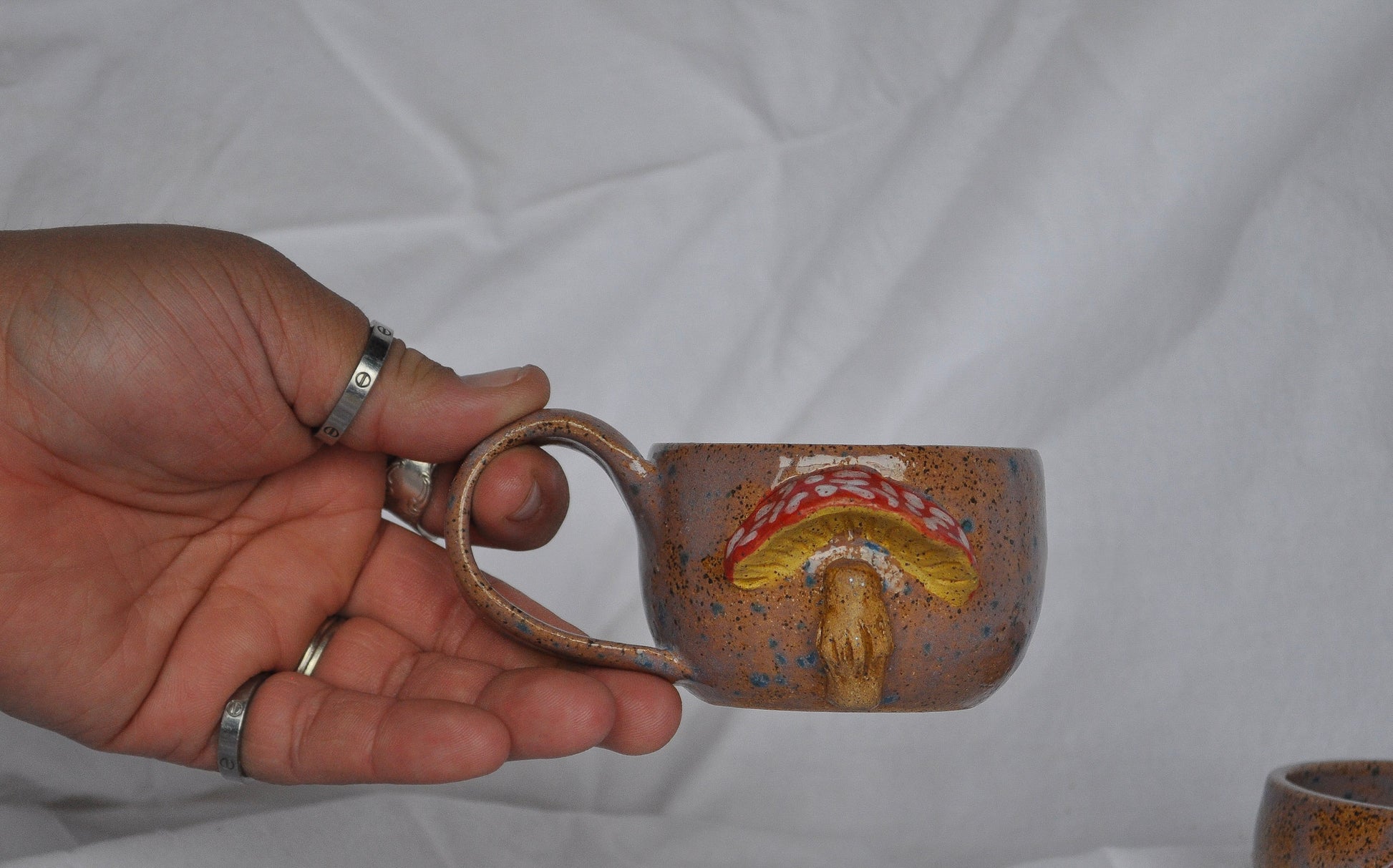 Hand holding a ceramic mug with a decorative design against a plain background
