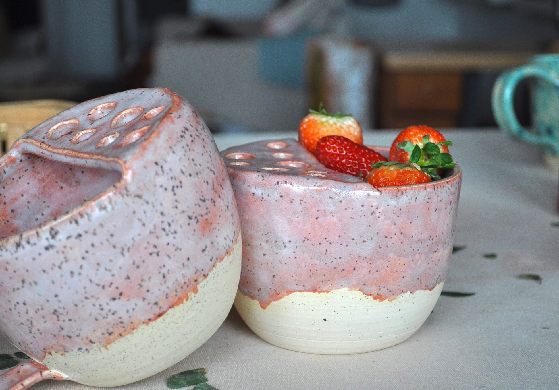 Two ceramic containers with a textured surface, one holding strawberries, on a blurred background.