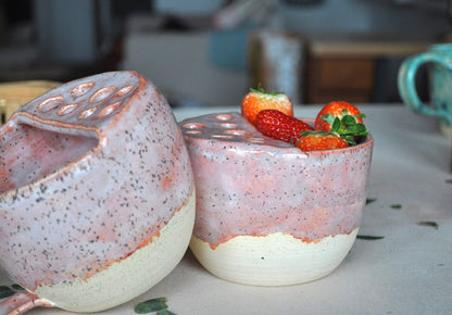 Two ceramic containers with a textured surface, one holding strawberries, on a blurred background.