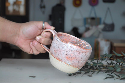 Hand holding a ceramic mug with speckled design on a blurred background