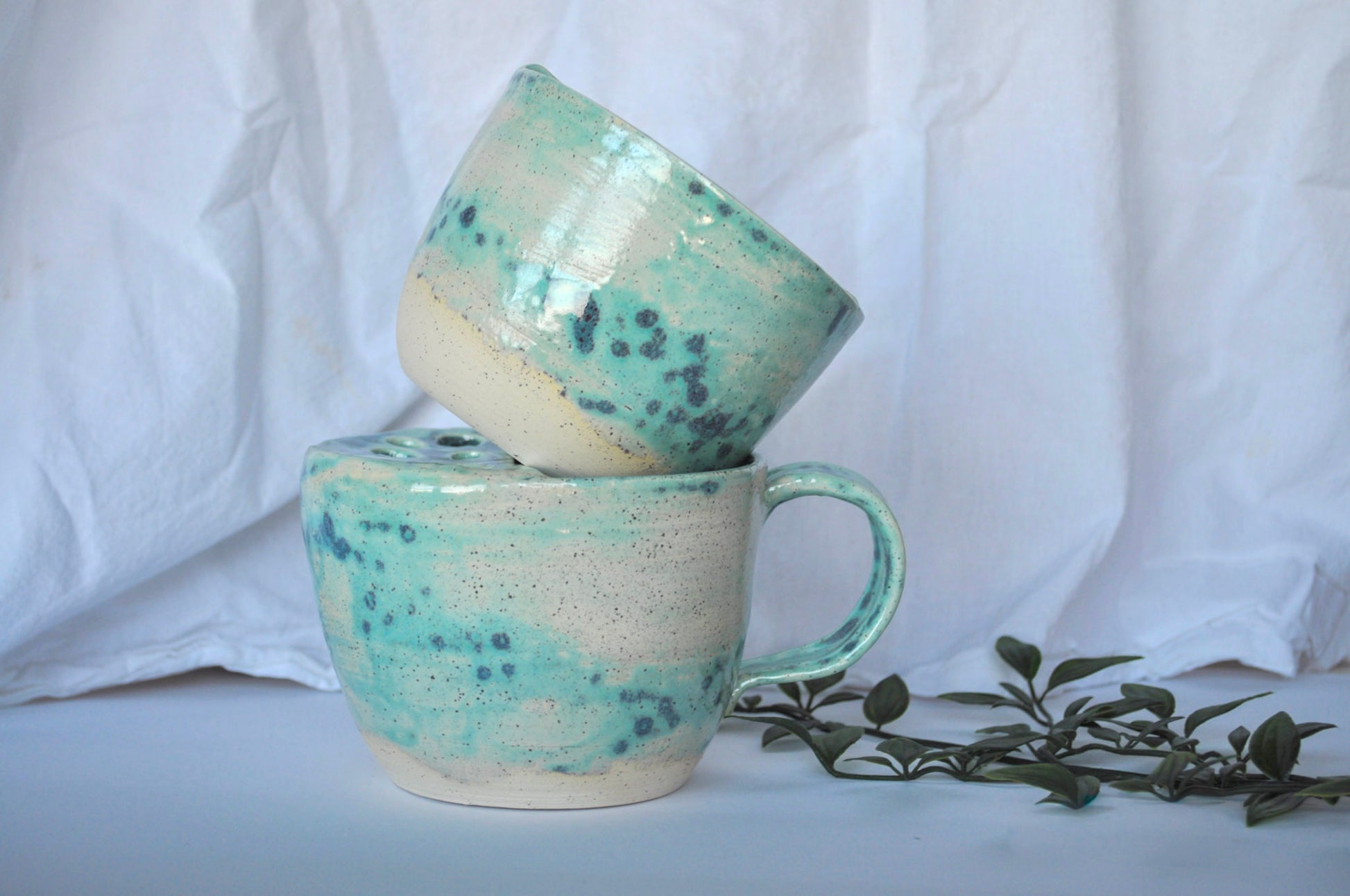 Two ceramic mugs with teal and white speckled glaze on a white background.