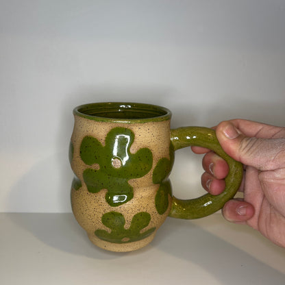 Hand holding a ceramic mug with green and beige design on a white background