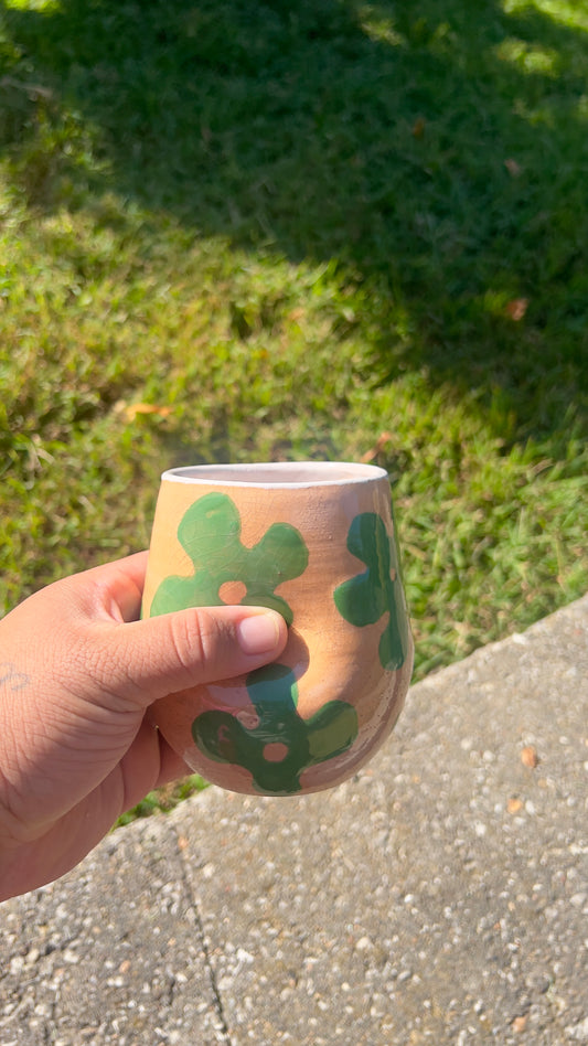 Hand holding a wooden cup with green patterns against a grassy background
