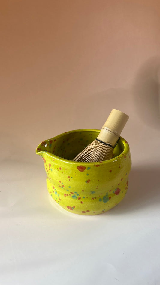 Green neon ceramic with colorful speckles and with a  wooden whisk  inside bowl on a white background