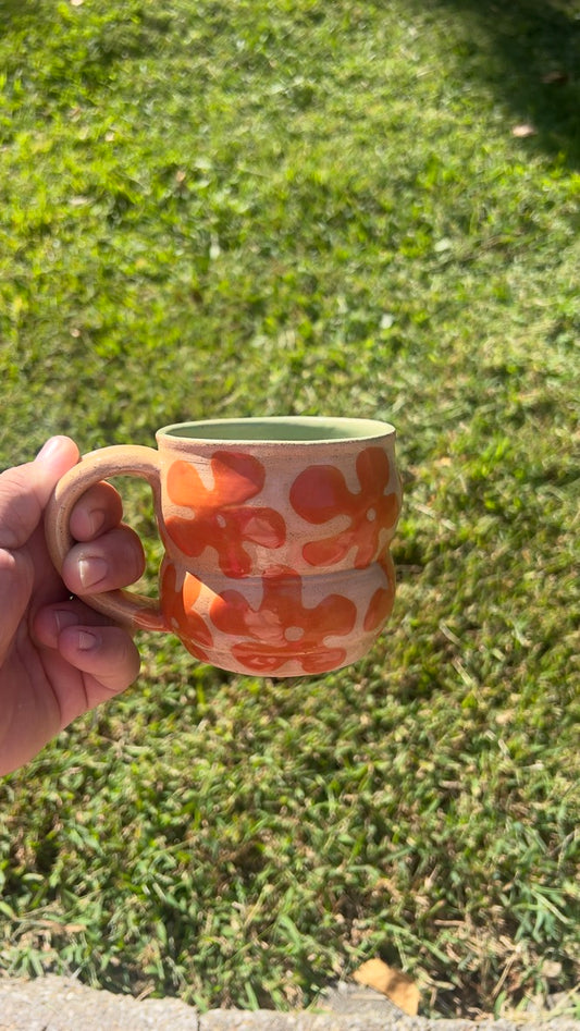 Hand holding a ceramic mug with floral pattern against a grassy background