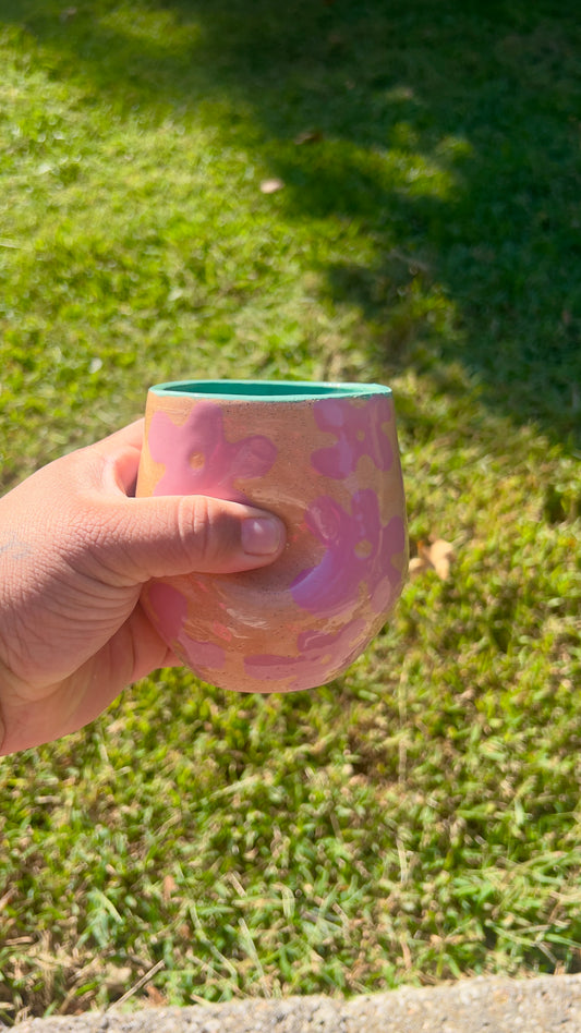 Hand holding a pink floral-patterned cup against a grassy background