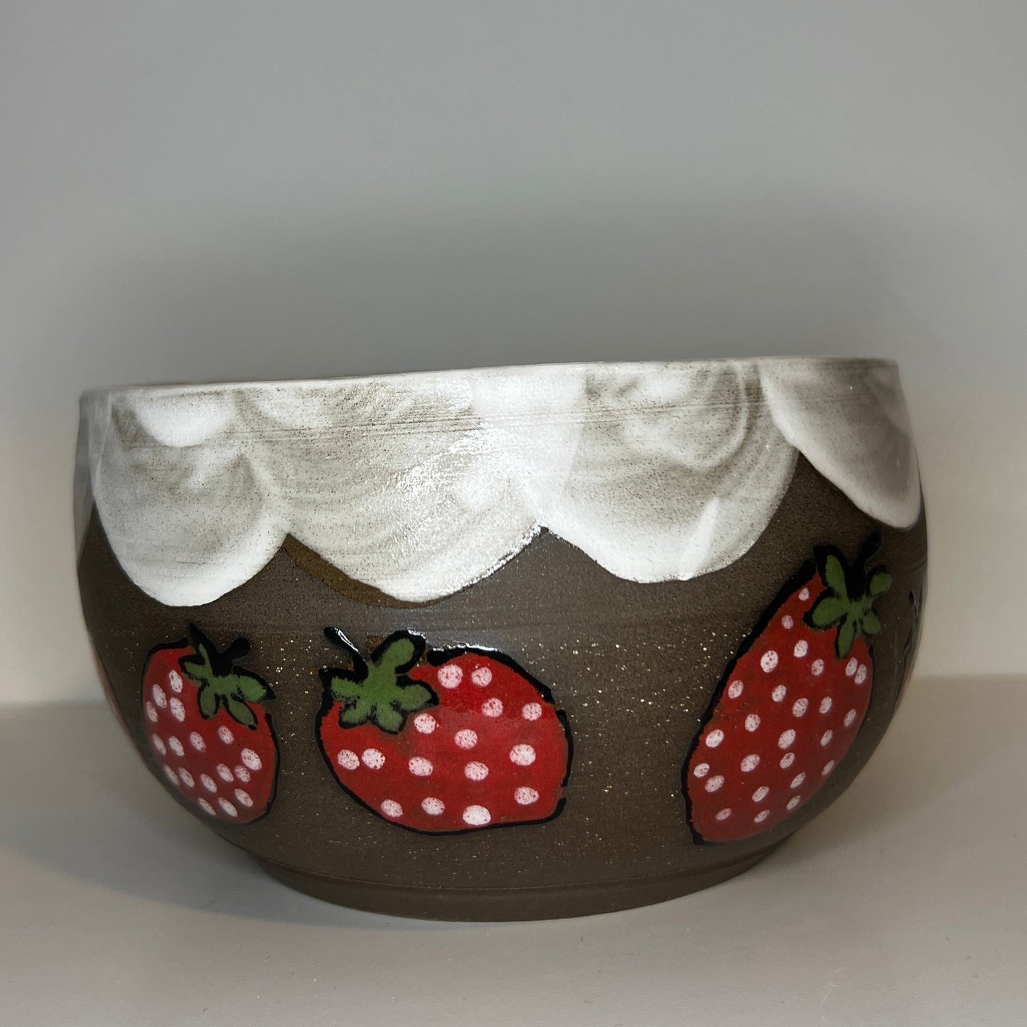 Dark brown ceramic bowl with strawberry designs and added with a red inside and The red rim features a hand-glazed swooping design that adds movement and visual interest. The bowl is against a white background