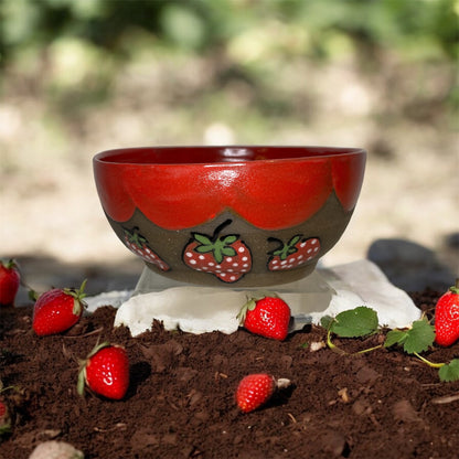 Dark brown ceramic bowl with strawberry designs and added with a red inside and The red rim features a hand-glazed swooping design that adds movement and visual interest. The bowl is
Outside with dirt and strawberries 