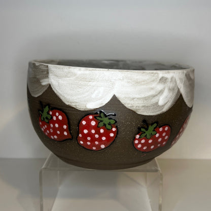 Dark brown ceramic bowl with strawberry designs and added with a white color inside and The white rim features a hand-glazed swooping design that adds movement and visual interest. The bowl is on a clear stand against a white background