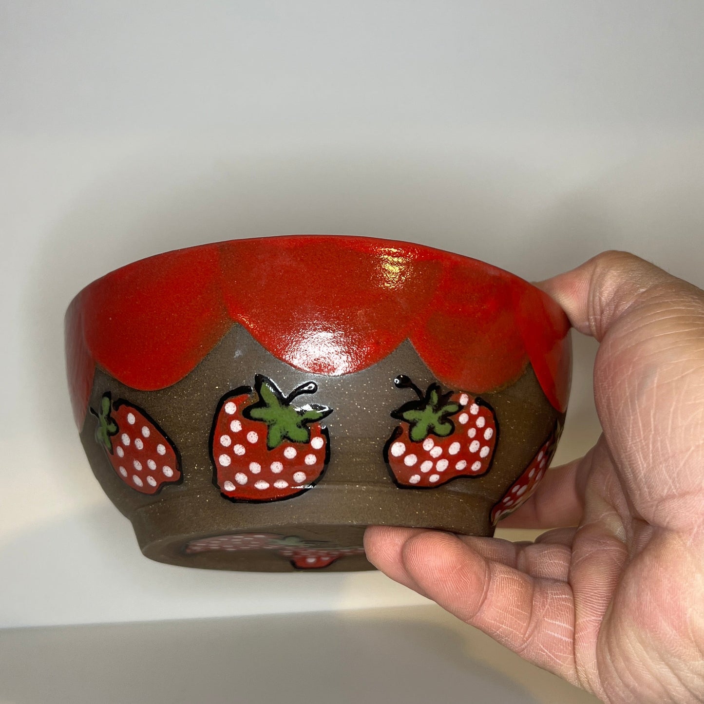Dark brown ceramic bowl with strawberry designs and added with a red inside and The red rim features a hand-glazed swooping design that adds movement and visual interest. The bowl is against a white background