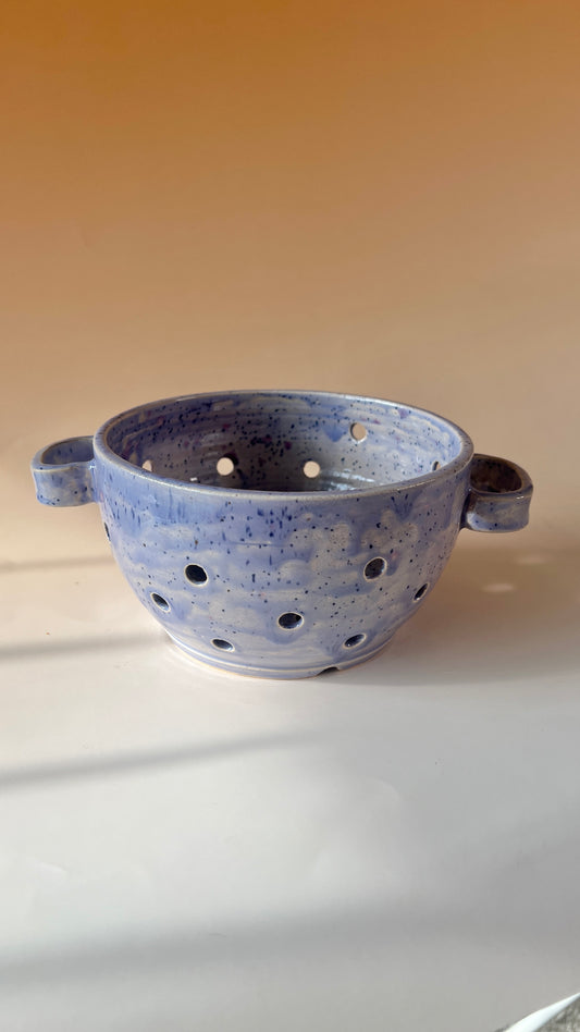 Blue ceramic colander with handles on a beige background