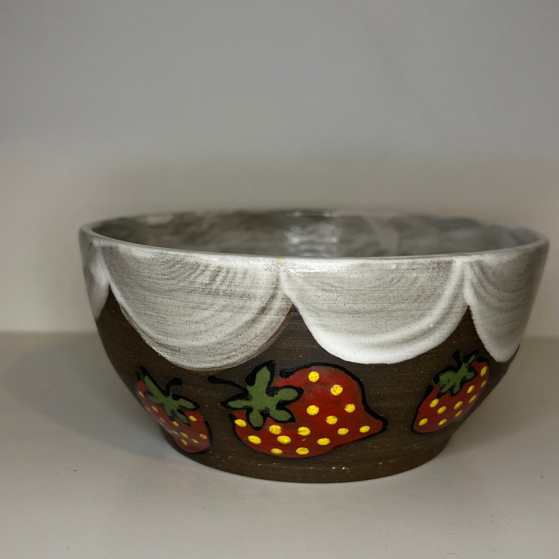 Dark brown ceramic bowl with strawberry designs and added with a white glaze inside and The white rim features a hand-glazed swooping design that adds movement and visual interest. The bowl is on a white background