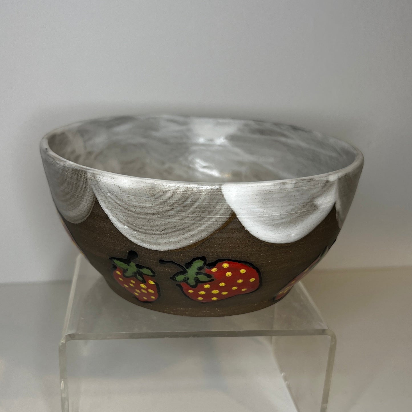 Dark brown ceramic bowl with strawberry designs and added with a white color inside and The white rim features a hand-glazed swooping design that adds movement and visual interest. The bowl is on a clear stand against a white background