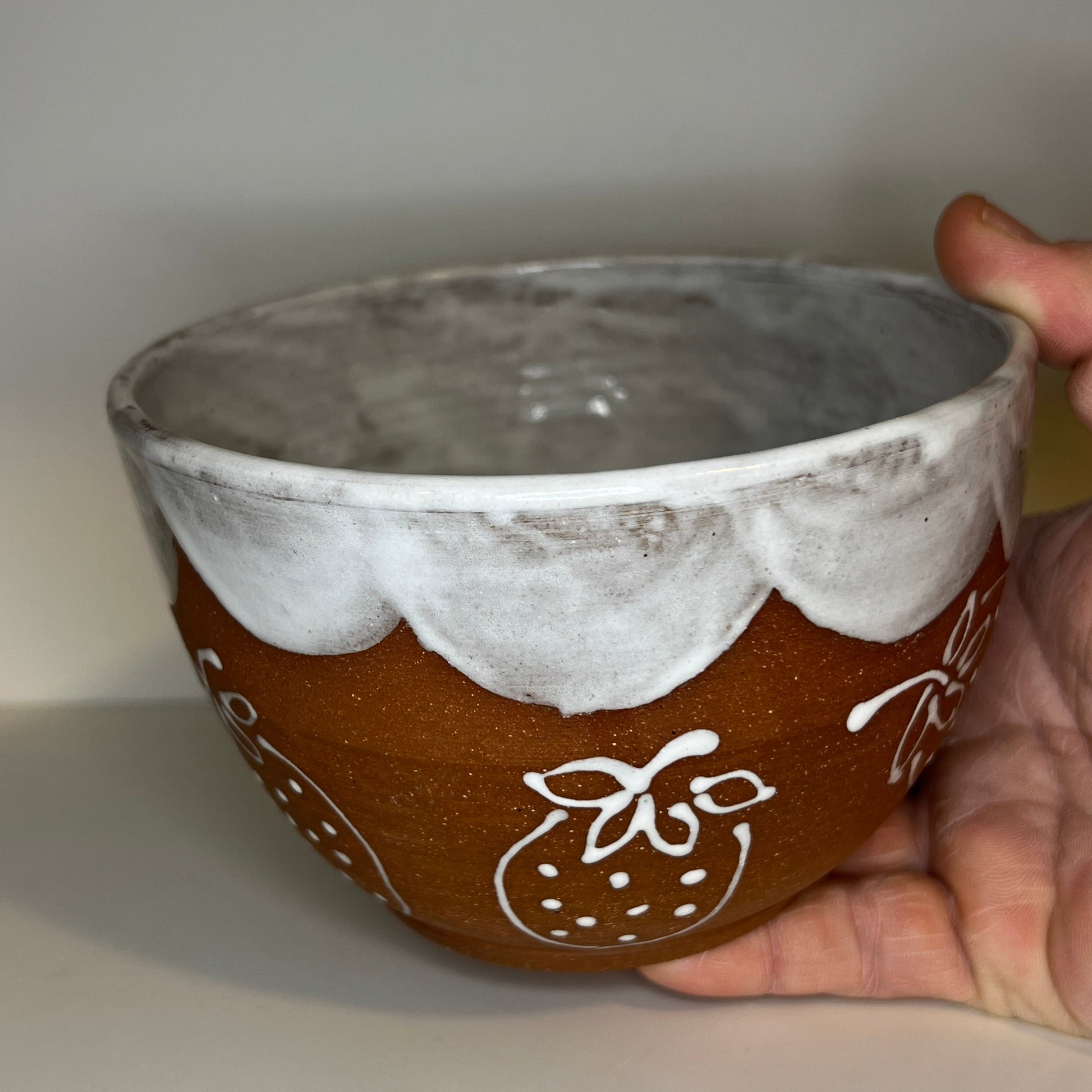 Ceramic bowl with decorative patterns held by a hand on a white surface