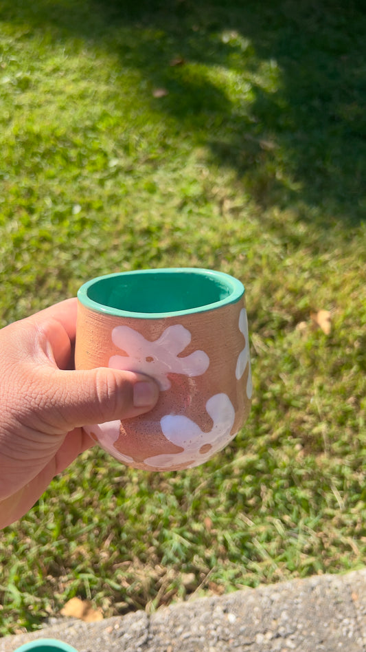 Hand holding a pink cup with white floral patterns against a grassy background