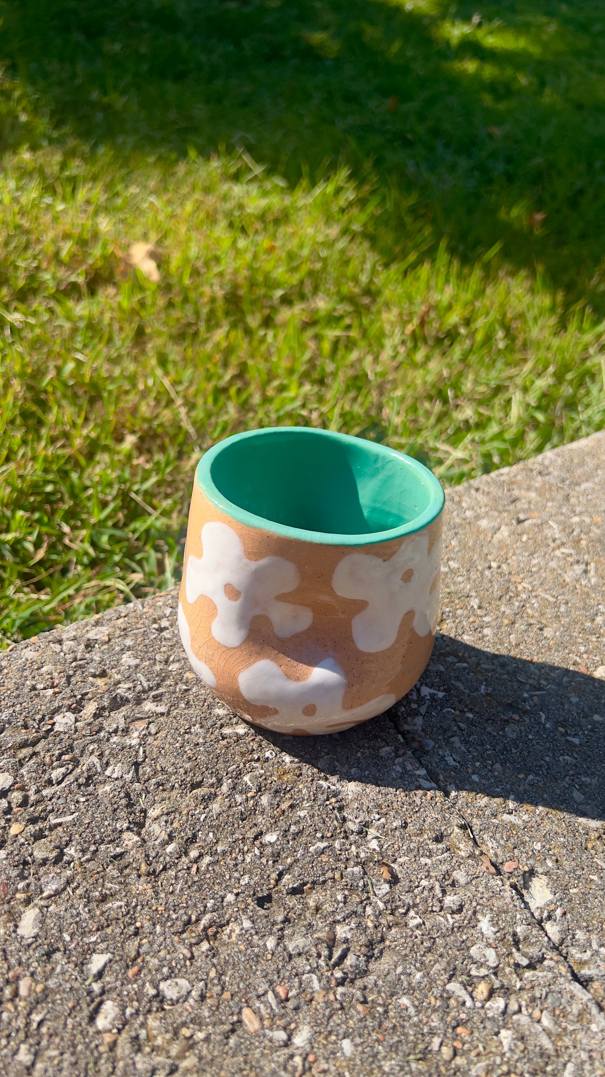 Ceramic mug with floral patterns on a concrete surface with grass in the background